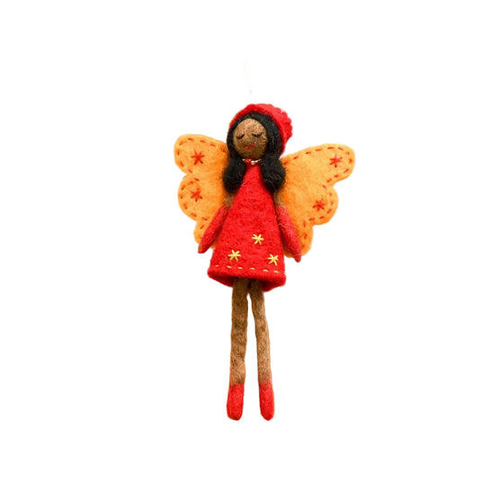 Small fairy doll with orange wings and a red dress hanging from a wooden stick on a white wooden background.