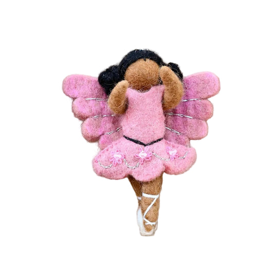Plush fairy toy with pink wings and dress on a wooden surface with green leaf decorations.