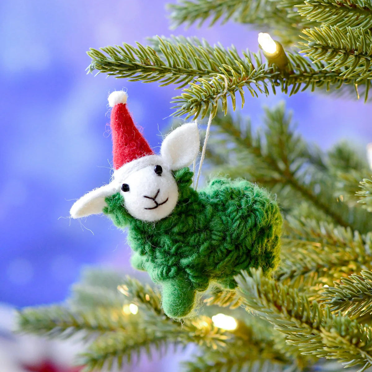 Knitted sheep ornament with a red hat hanging on a Christmas tree.